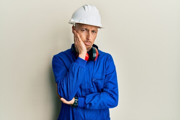 Bald man with beard wearing builder jumpsuit uniform and hardhat thinking looking tired and bored with depression problems with crossed arms.