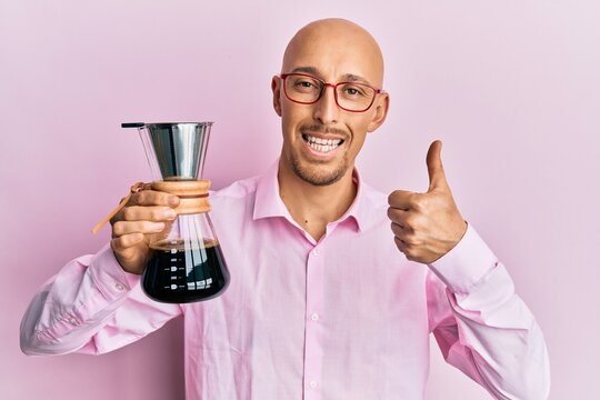 Bald man with beard holding coffee maker with filter smiling happy and positive, thumb up doing excellent and approval sign