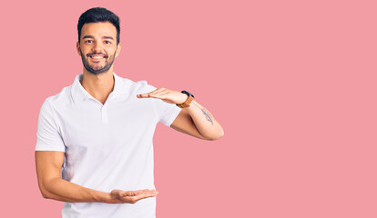 Young handsome hispanic man wearing casual clothes gesturing with hands showing big and large size sign, measure symbol. smiling looking at the camera. measuring concept.