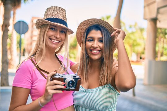 Two beautiful and young girl friends together having fun at the city standing with vintage camera