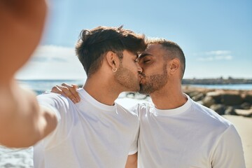 Young gay couple smiling happy making selfie by the smartphone at the beach.