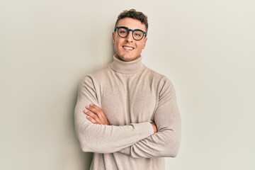Hispanic young man wearing casual turtleneck sweater happy face smiling with crossed arms looking at the camera. positive person.