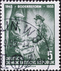 GERMANY, DDR - CIRCA 1955 : a postage stamp from Germany, GDR showing a farmer with a flat cap who receives his deed of ownership after the land reform. Text: 10 years of land reform