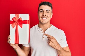 Hispanic young man holding gift smiling happy pointing with hand and finger