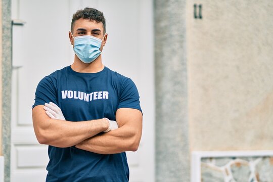 Young Hispanic Volunteer Man With Arms Crossed Wearing Medical Mask At The City.