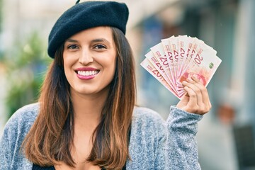Young latin woman wearing french style holding israel shekels at the city.
