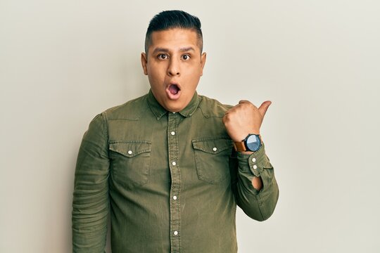 Young latin man wearing casual clothes surprised pointing with hand finger to the side, open mouth amazed expression.