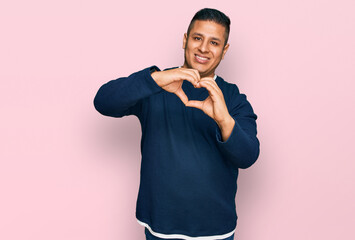 Young latin man wearing casual clothes smiling in love doing heart symbol shape with hands. romantic concept.