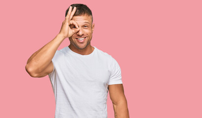Fototapeta na wymiar Handsome muscle man wearing casual white tshirt doing ok gesture with hand smiling, eye looking through fingers with happy face.