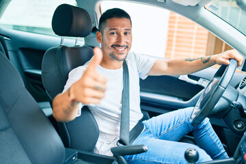 Young hispanic man smiling happy doing ok sign driving car.