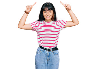 Young hispanic girl wearing casual clothes smiling amazed and surprised and pointing up with fingers and raised arms.