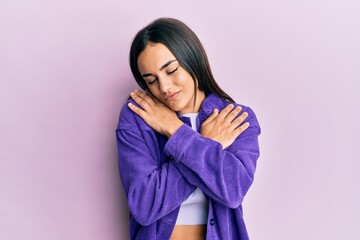 Fototapeta premium Young brunette woman wearing casual clothes hugging oneself happy and positive, smiling confident. self love and self care