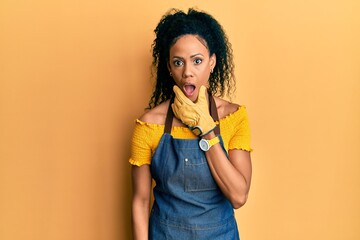 Middle age african american woman wearing professional apron looking fascinated with disbelief, surprise and amazed expression with hands on chin