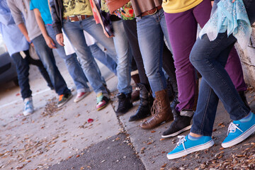 crowd of young adults with attitude wearing jeans standing in a line. Shot from waist down. No faces