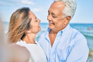 Middle age hispanic couple smiling happy making selfie by the camera at the beach.