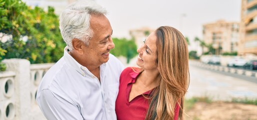 Obraz premium Middle age hispanic couple smiling happy and hugging walking at street.