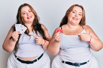 Plus size caucasian sisters woman holding poker chips and cards smiling happy pointing with hand and finger