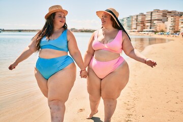 Two plus size overweight sisters twins women happy and proud of their bodies walking at the beach...