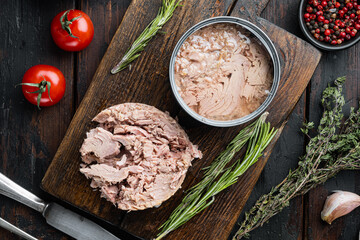 Tuna in a can, whole and chopped, on wooden cutting board, on old dark  wooden table background....