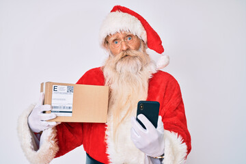 Old senior man with grey hair and long beard wearing santa claus costume holding delivery box and phone clueless and confused expression. doubt concept.