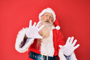 Old senior man with grey hair and long beard wearing traditional santa claus costume afraid and terrified with fear expression stop gesture with hands, shouting in shock. panic concept.
