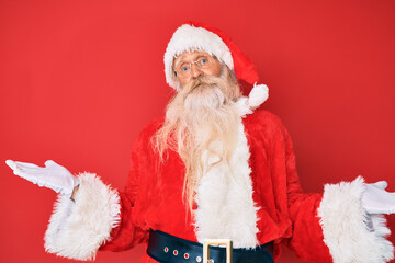 Old senior man with grey hair and long beard wearing traditional santa claus costume clueless and...