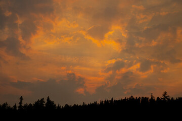Smokey sunset in the mountains of orange and purple clouds in the sky with silhouette of mountains and pine trees