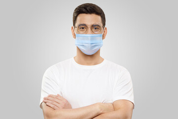 Handsome young man wearing white t-shirt and medical mask, isolated on gray background