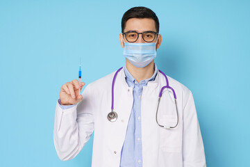 Young male doctor holding syringe with covid vaccine, ready to do coronavirus vaccination, isolated on blue background