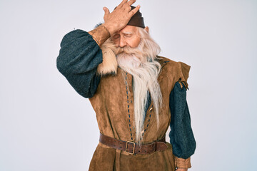 Old senior man with grey hair and long beard wearing viking traditional costume surprised with hand...