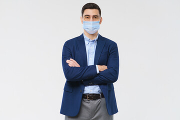 Young business man wearing medical mask, standing with crossed arms isolated on gray background