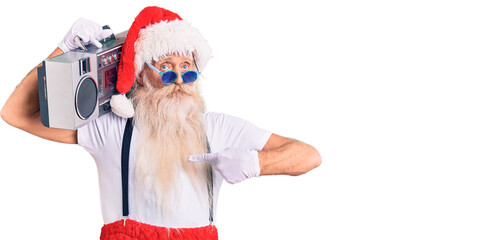 Old senior man with grey hair and long beard wearing santa claus costume and boombox pointing finger to one self smiling happy and proud