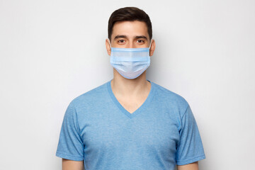 Young handsome man wearing blue t-shirt and medical mask, standing isolated on gray background