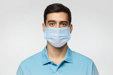 Young handsome man wearing blue polo shirt and medical mask, standing isolated on gray background