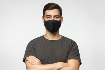 Young handsome man wearing grey t-shirt and black mask, standing with crossed arms, isolated on gray background