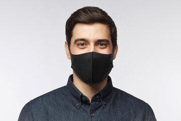 Young man wearing denim shirt and black mask standing isolated on gray background