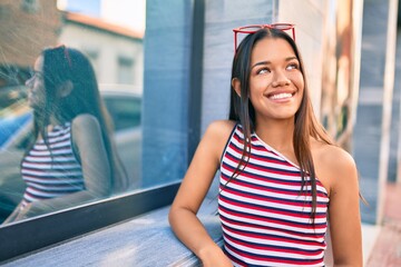 Young latin girl smiling happy leaning on the wall at the city.