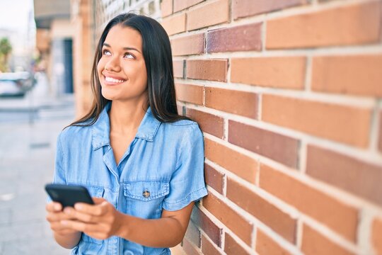 Young latin girl smiling happy using smartphone at the city.