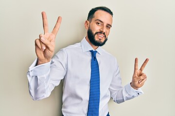 Young man with beard wearing business tie smiling looking to the camera showing fingers doing victory sign. number two.