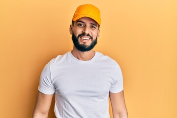 Young man with beard wearing yellow cap with a happy and cool smile on face. lucky person.