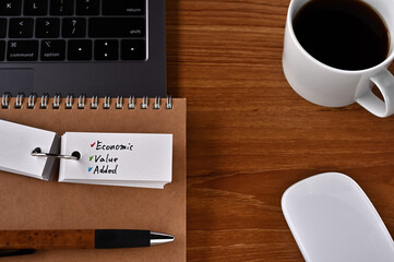 On the desk there is a laptop, a cup of coffee, and a word book with the word EVA written on it. It was an abbreviation for Economic Value Added.