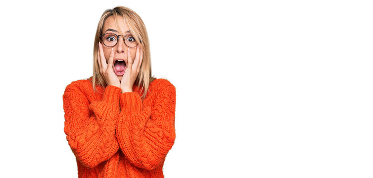 Beautiful blonde woman wearing casual clothes and glasses afraid and shocked, surprise and amazed expression with hands on face