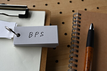 On the desk there is a clipboard, a notebook, and a word book with the word BPS written on it. It...