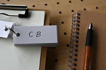 On the desk there is a clipboard, a notebook, and a word book with the word CB written on it. It...