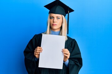 Beautiful blonde woman wearing graduation cap and ceremony robe holding blank banner clueless and...