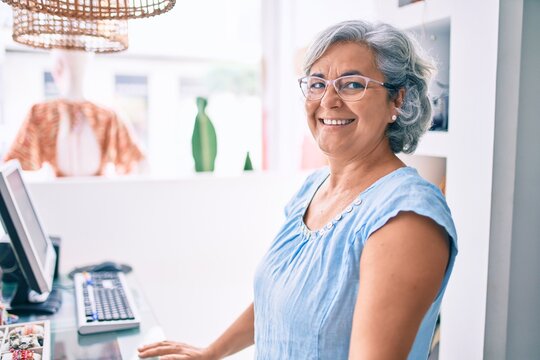 Middle age shop assistance woman working at the counter of retail shop smiling happy