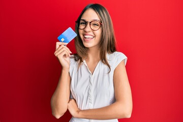 Young brunette woman holding credit card smiling and laughing hard out loud because funny crazy...