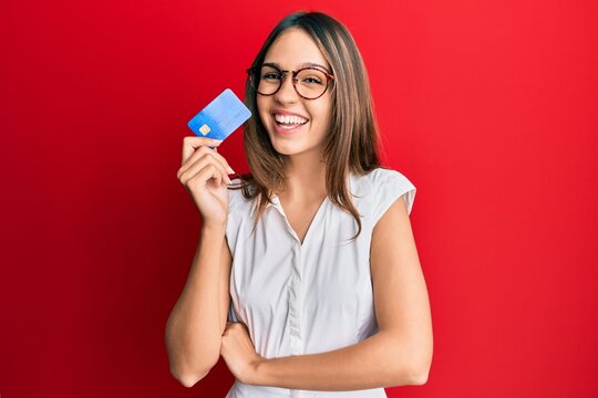 Young brunette woman holding credit card smiling and laughing hard out loud because funny crazy joke.