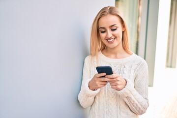 Naklejka premium Young blonde girl smiling happy using smartphone at the city.