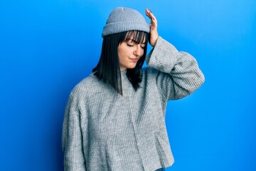Young hispanic woman wearing wool sweater and winter hat surprised with hand on head for mistake,...
